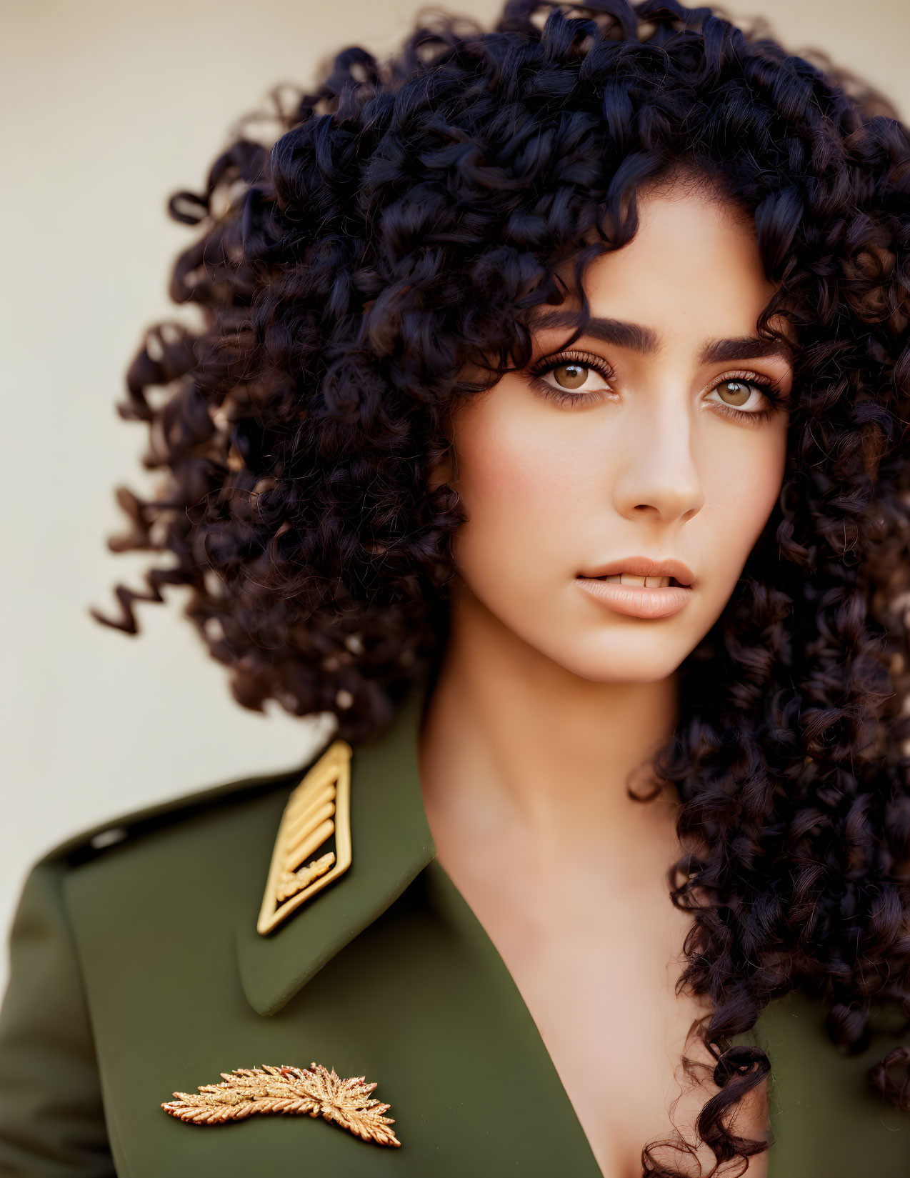 Woman with curly black hair and military-style jacket featuring gold epaulets