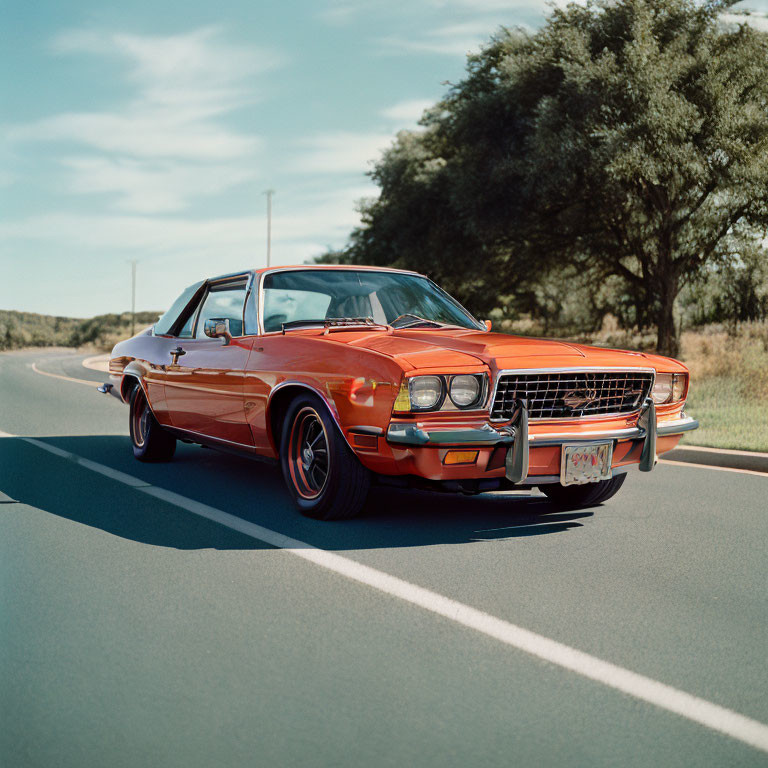 Vintage orange muscle car with chrome details on asphalt road in nature under blue sky