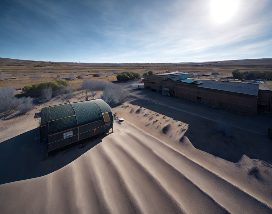 Semi-truck parked near warehouses with sand dunes and clear sky