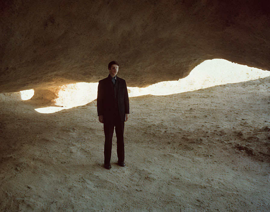 Person in suit standing in sandy cave with natural light openings