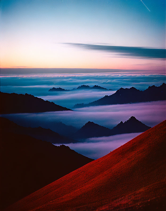 Twilight sky with stars over shadowy mountain peaks and red foreground glow