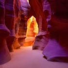 Person with backpack in narrow sandstone canyon with warm red and orange hues.