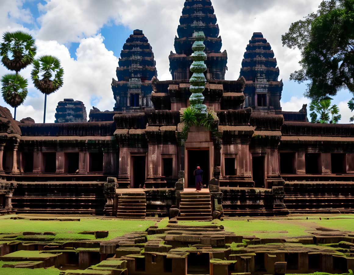 Intricate carvings on ancient temple with rising spires and greenery under blue sky.