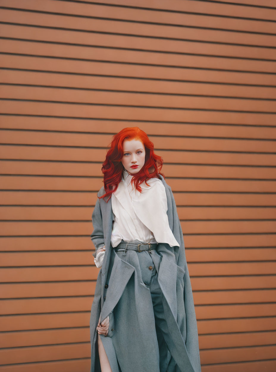 Red-haired woman in white blouse and overcoat against striped brown wall