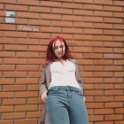 Red-haired woman in white blouse and overcoat against striped brown wall