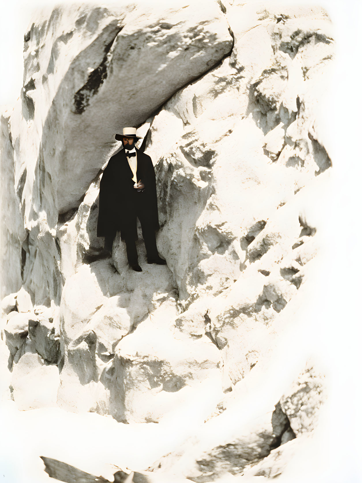 Person in Black Suit and White Hat Standing Among Rugged Rocks