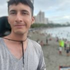 Young man in light grey shirt on rocky beach under overcast sky