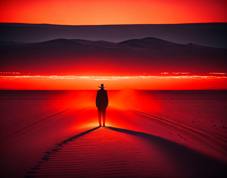 Silhouette of person in hat on desert dune at red sunset