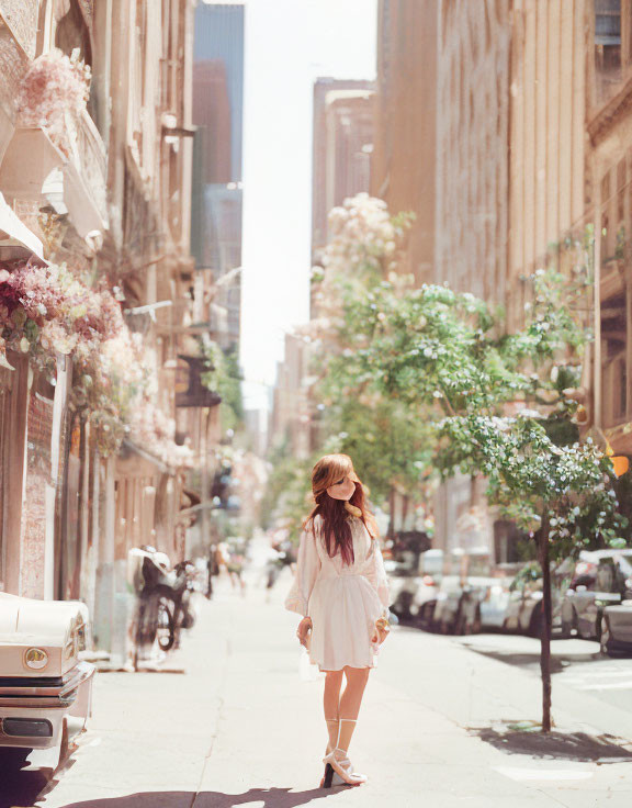 Woman in white dress strolling city street with blooming trees
