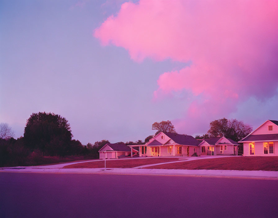 Suburban street at dusk with houses under vibrant pink sky