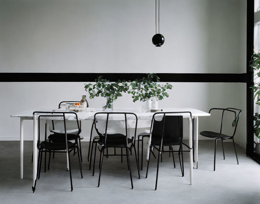 Minimalistic Dining Room with White Table, Black Chairs, Pendant Light, and Plant Centerpiece