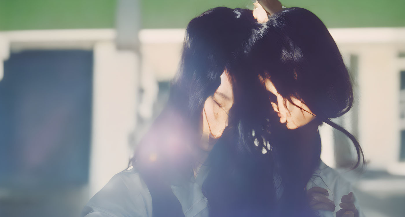 Dark-haired individuals touching foreheads in soft sunlight.