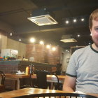 Gray-bearded man smiling at rustic table with steaming dishes under warm lights