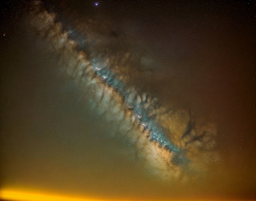 Starry night sky with Milky Way galaxy and amber-hued clouds