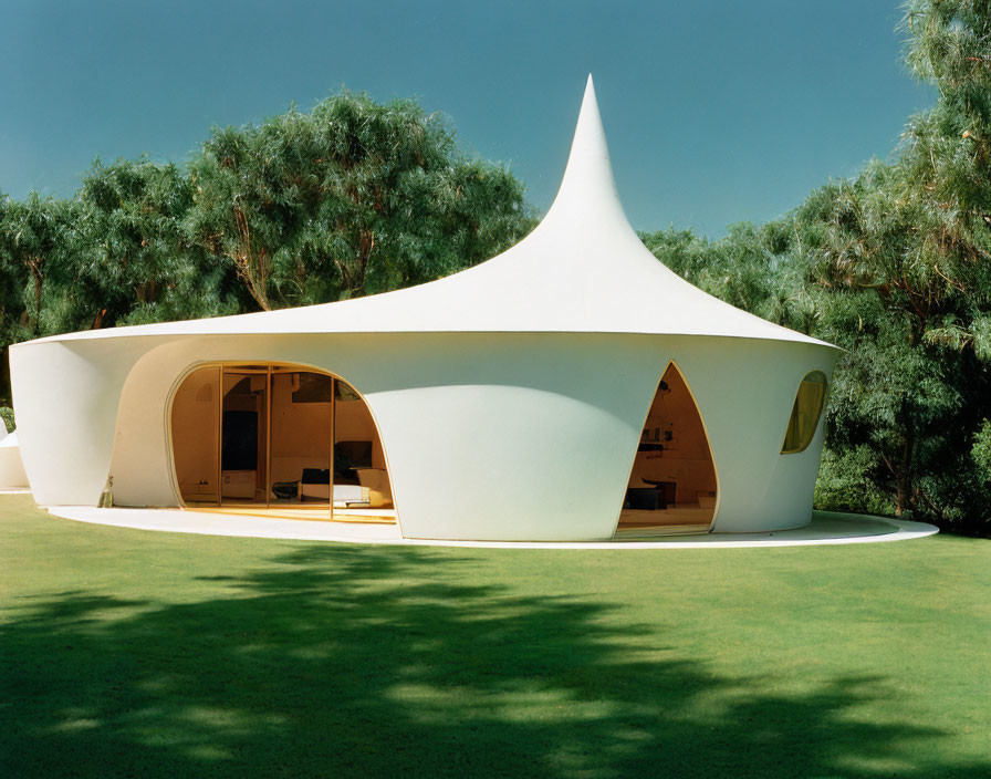 Modern house with flowing white tent-like roof and rounded walls in lush green setting