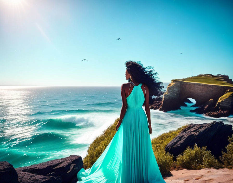 Woman in teal dress on coastal cliff gazes at ocean