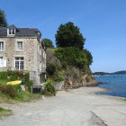 Stone facade seaside cottage with manicured gardens and sailboats under clear blue sky