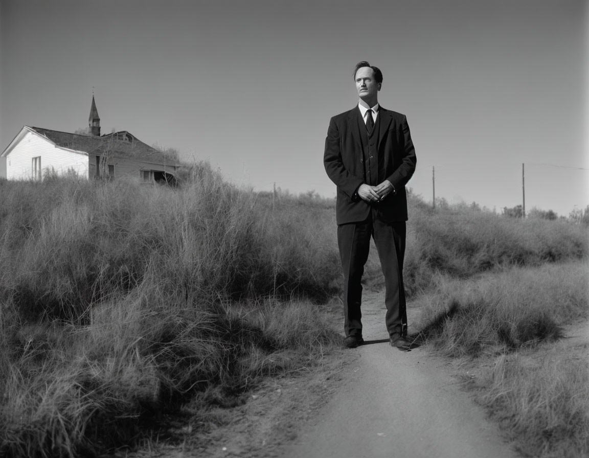 Man in suit standing on dirt road with church and clear skies