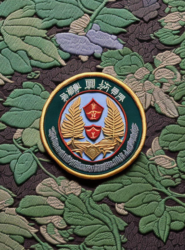 Embroidered patch with shield, star, wings, wheat, and Chinese characters on green foliage.