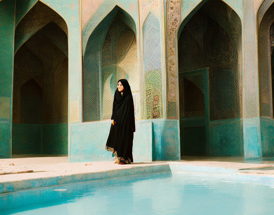 Woman in black hijab near turquoise water by ornate Persian mosque wall