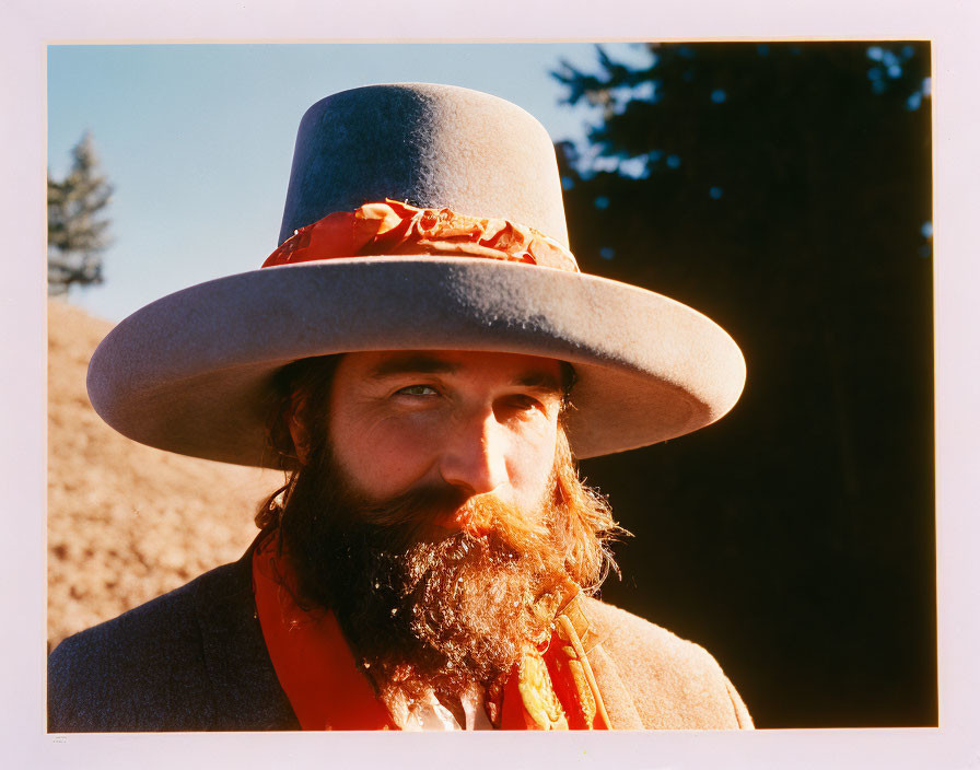 Bearded person in wide-brimmed hat with red bandana in sunny natural setting