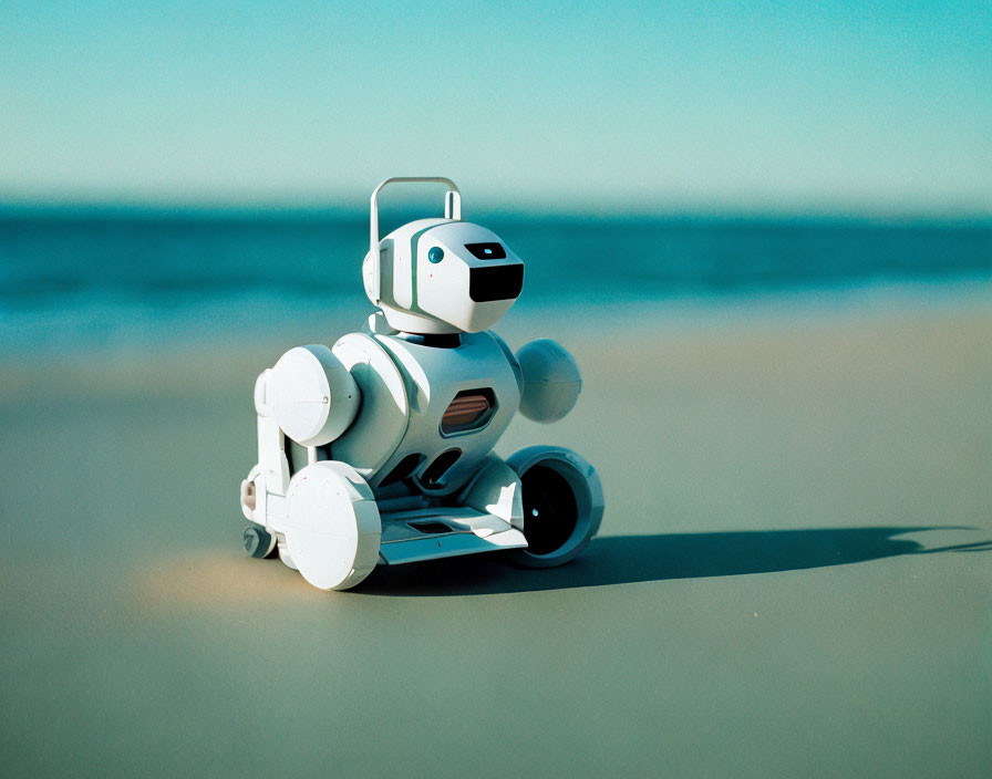 Small White Robot on Sandy Beach Under Clear Blue Sky