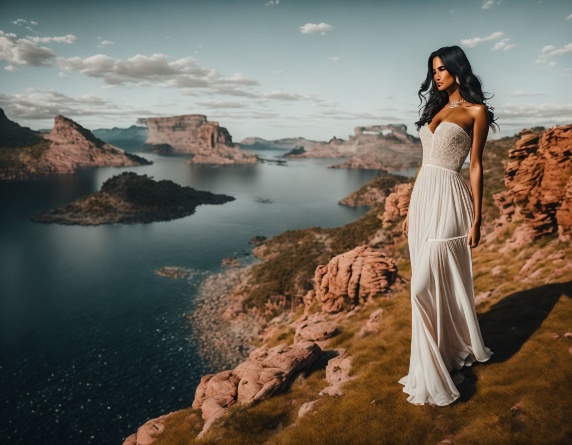 Woman in white dress on rocky overlook with serene lake and mountains.