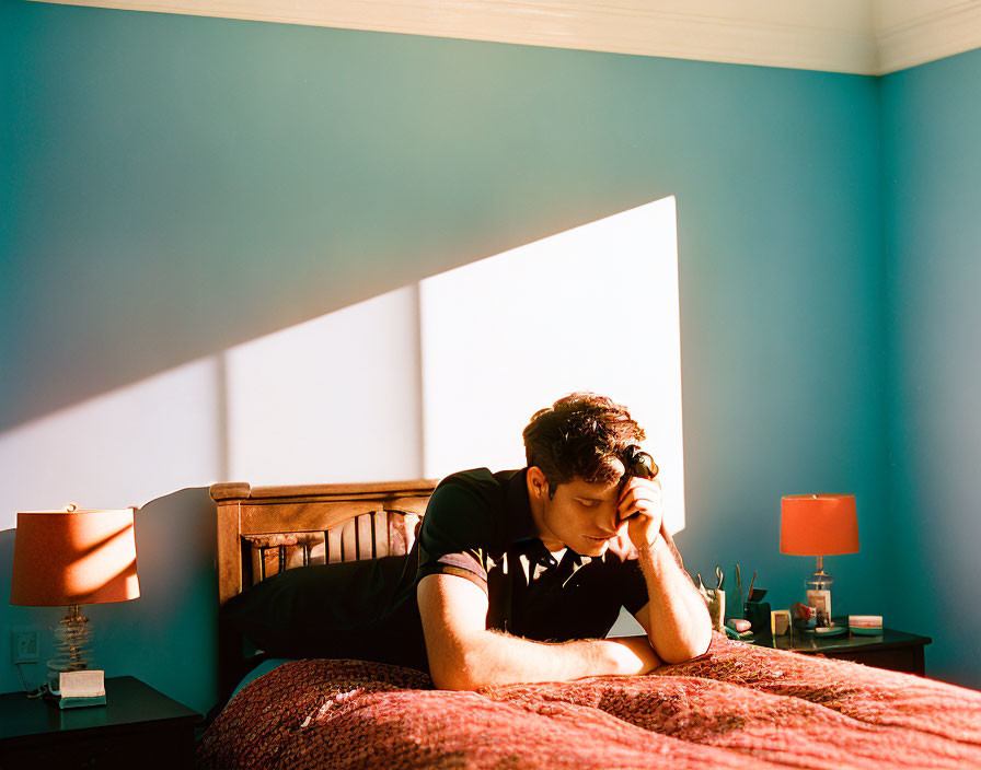 Person resting on bed in sunlit room with blue walls and bedside tables