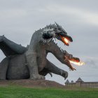 Multi-headed dragon sculpture breathing fire in grassy field against cloudy sky