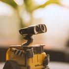 Yellow wheeled robot with binocular eyes in sandy environment.