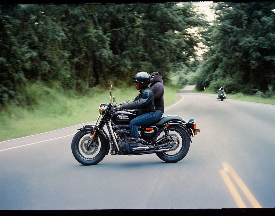 Motorcyclist in helmet and jacket rides chopper-style bike on curving road