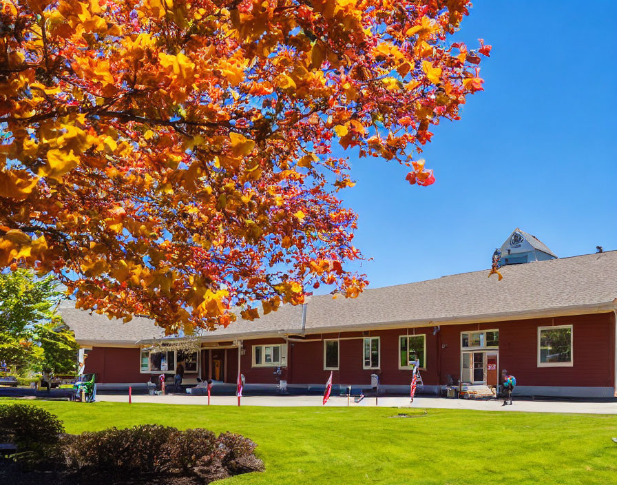 Colorful autumn scene with red school building, students, and adults under clear blue sky