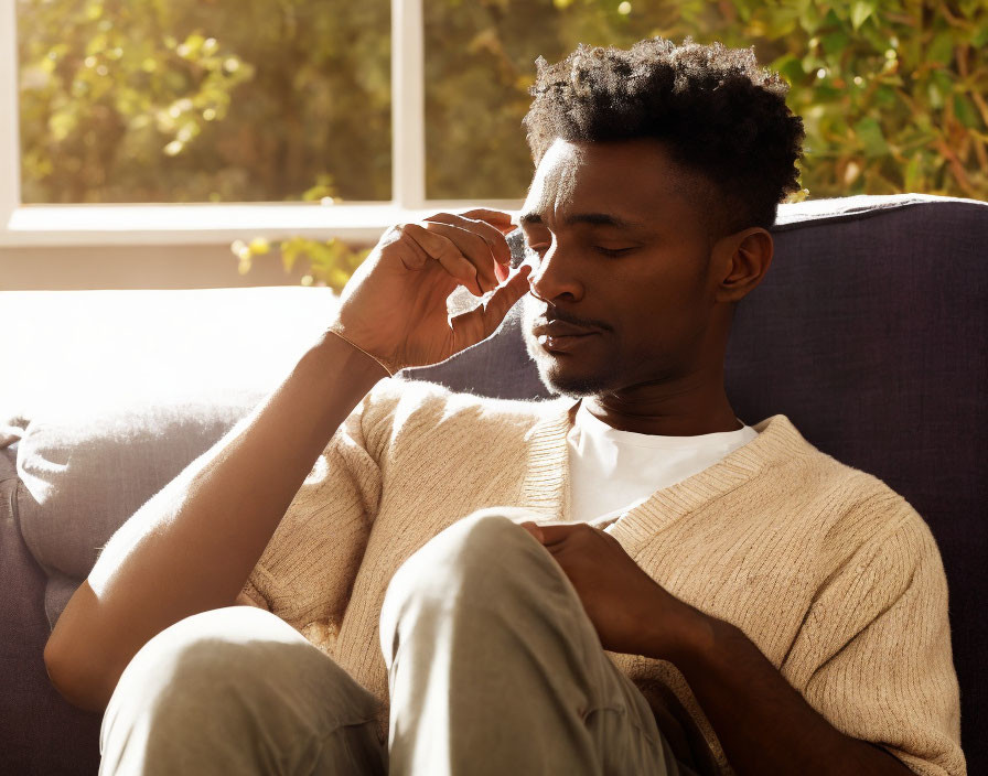 Man in white sweater and grey pants sitting on couch in warm sunlight.