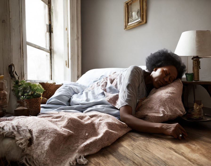 Woman peacefully napping on warmly lit wooden floor with pillows & houseplants