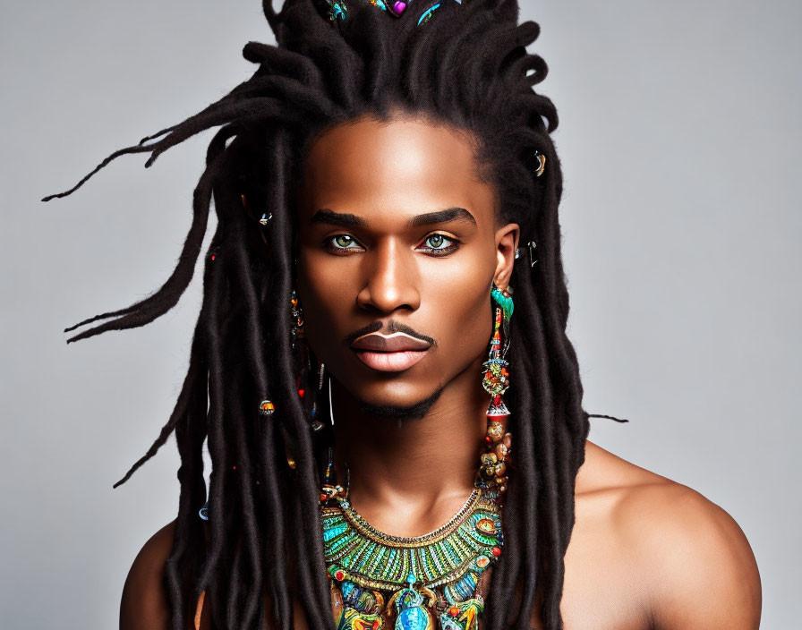 Portrait of person with long dreadlocks, beads, earrings, and necklace on gray background
