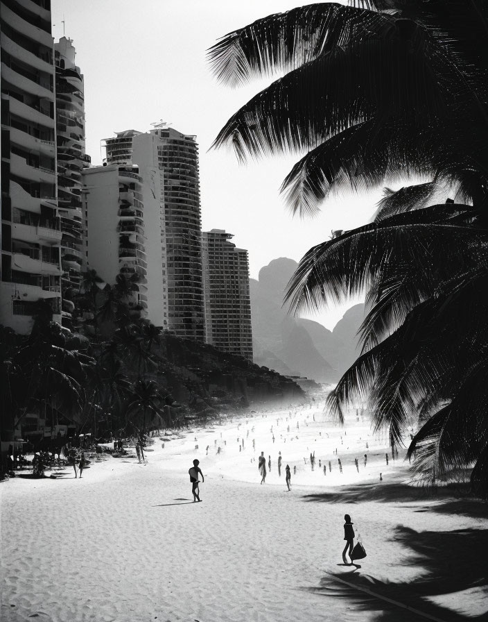 Monochrome image of people on sunlit beach with tall buildings and palm trees