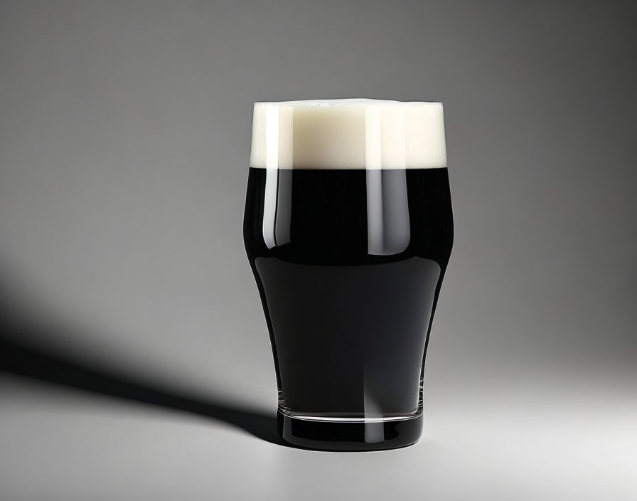 Dark Stout Beer Glass with Creamy Head on Gray Background