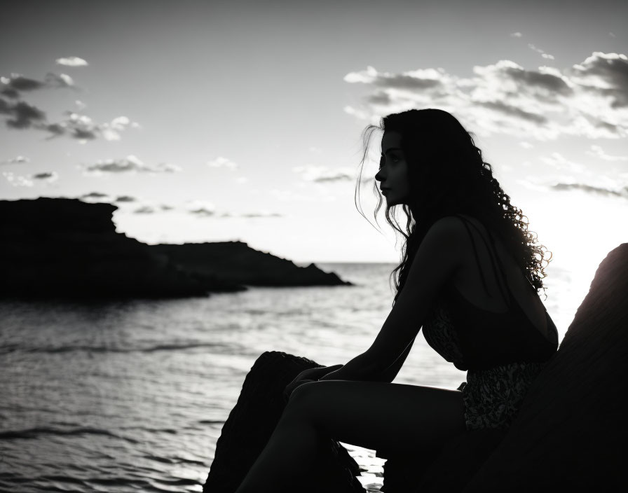 Silhouette of person on rock gazing at sunset over ocean