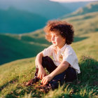 Curly-Haired Child Sitting on Green Hillside at Golden Hour