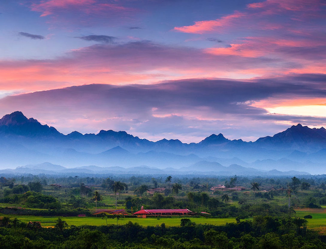 Colorful sunset over green landscape with red-roofed building and misty mountains