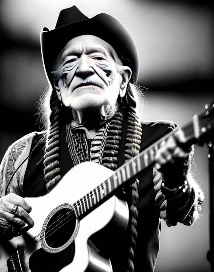 Elderly man with braided hair in cowboy hat and bandana plays guitar