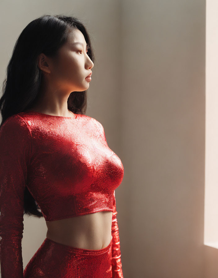 Woman in Red Lace Top Poses Against Sunlit Wall