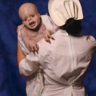 Woman in White Floral Outfit Holding Cheerful Baby on Blue Background