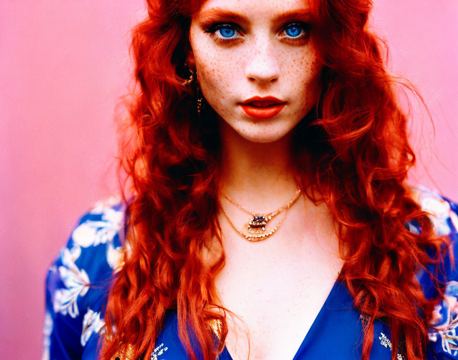 Red-haired woman with freckles in blue floral outfit on pink background