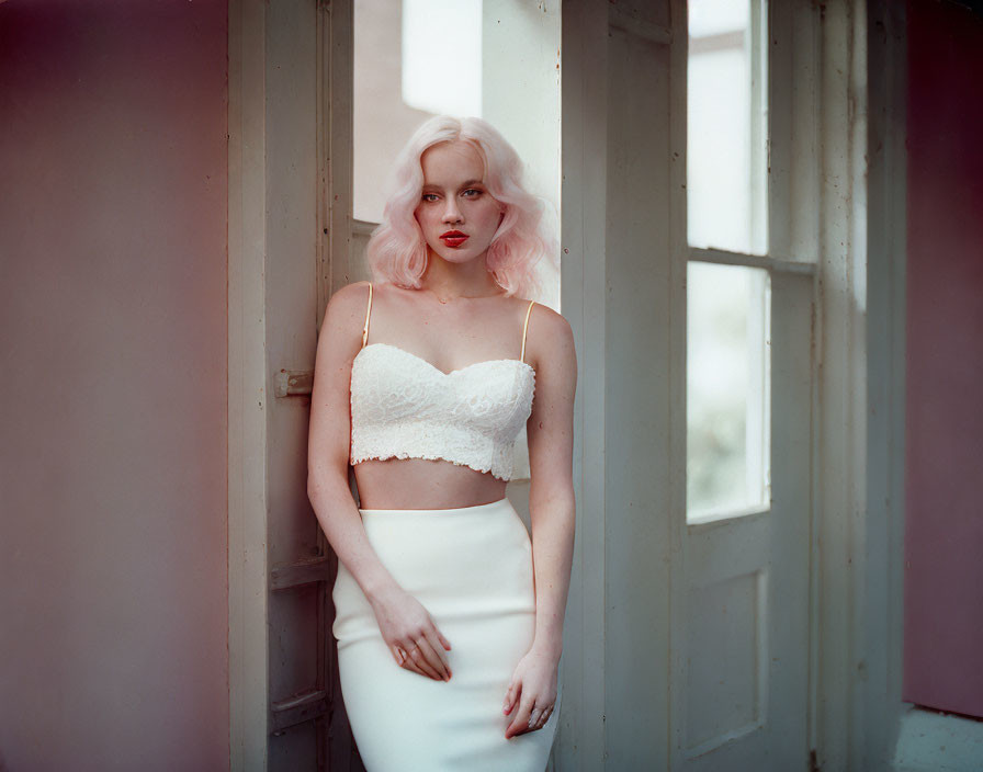 Pink-haired woman in white lace outfit by a door with dreamy expression