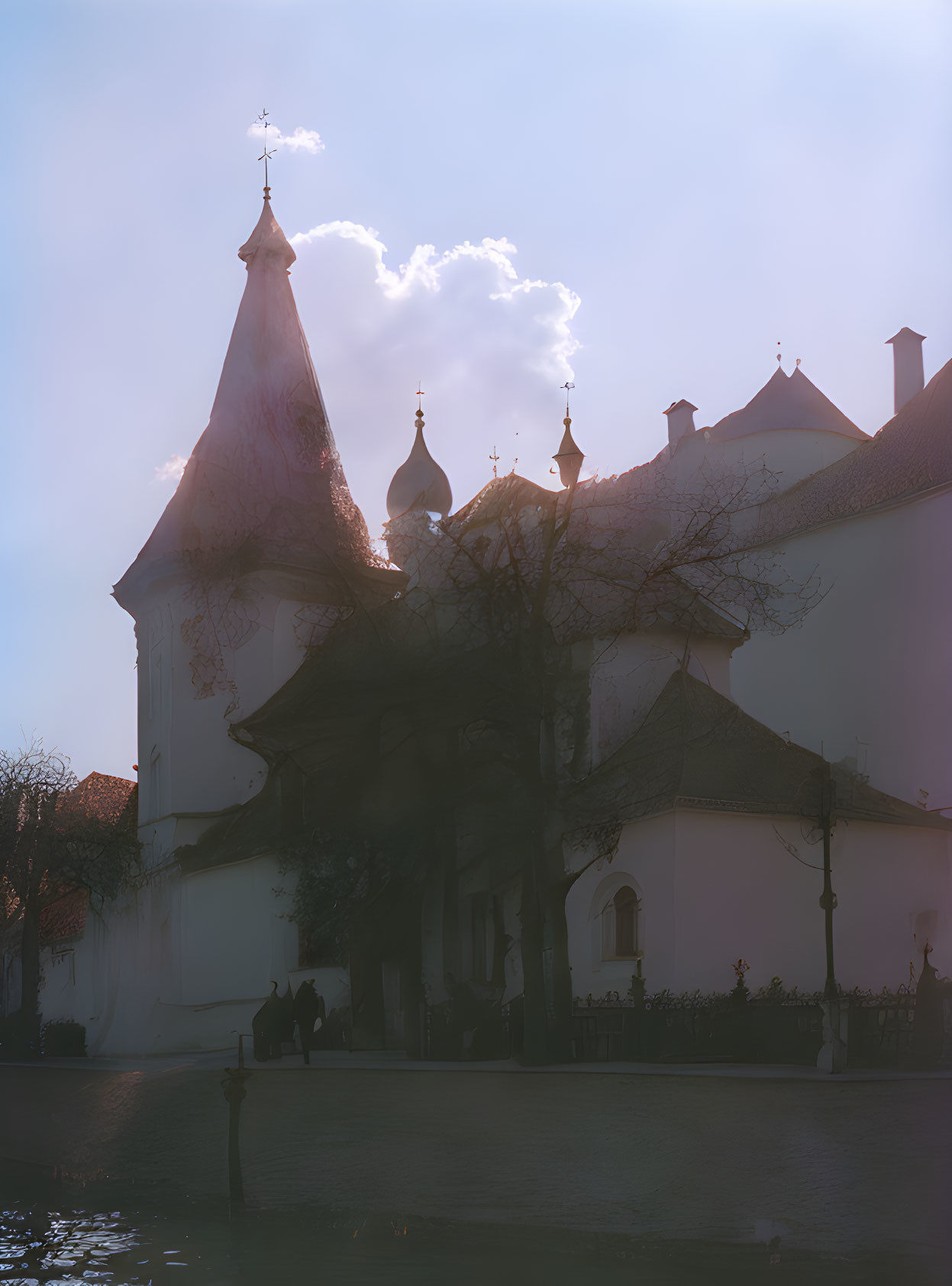 Historical building with spired towers in soft sunlight and silhouettes of people.