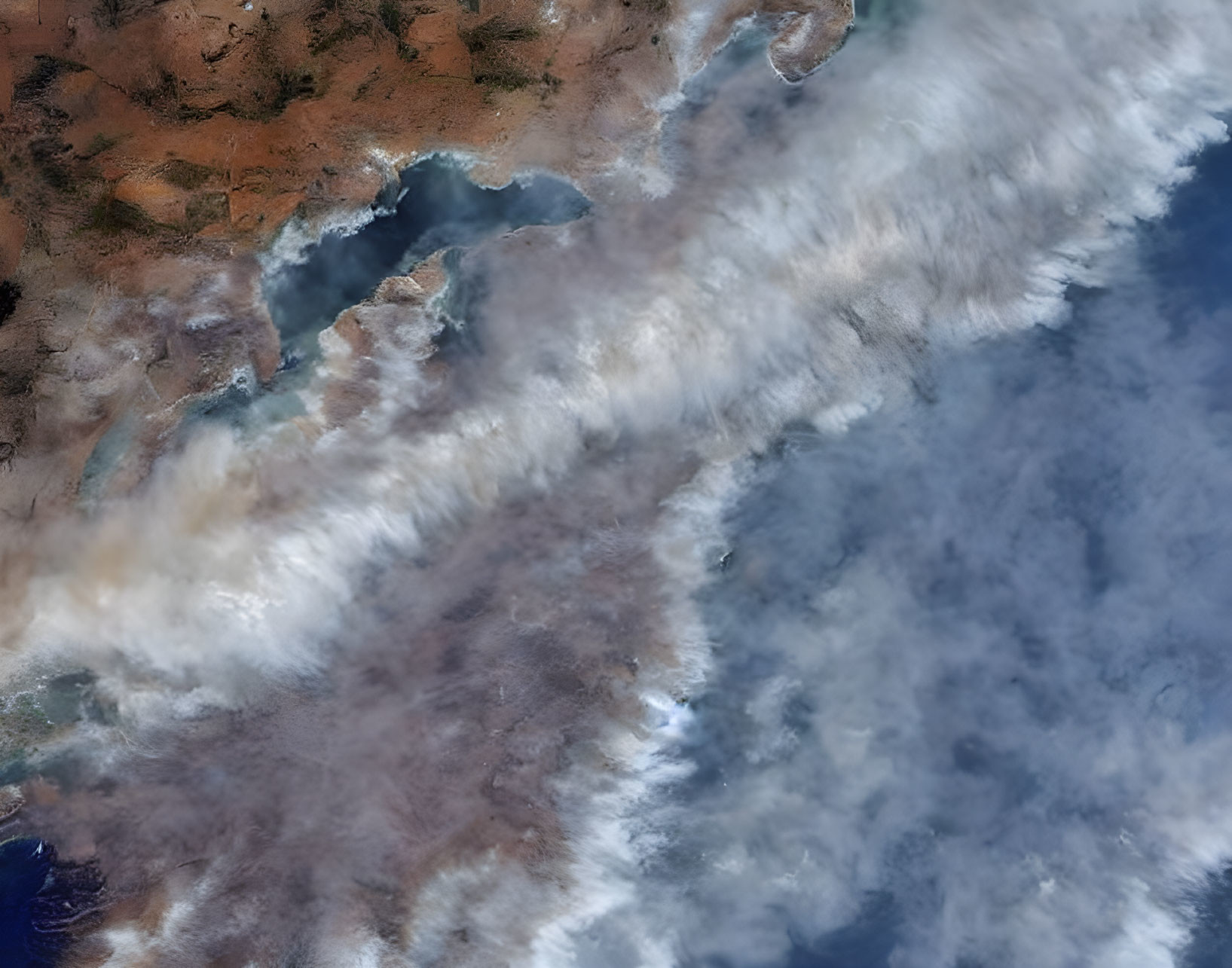 Satellite image of smoke spreading over landscape with visible landforms.