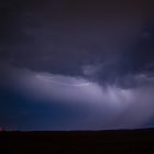 Giant shelf cloud with lightning bolts over lone tree in night sky