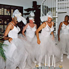 Three women in elegant white dresses with decorative hair accessories in vintage attire posed against a floral background.