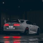 Black Sports Car with Illuminated Headlights and Red Brake Lights Against Dark Background